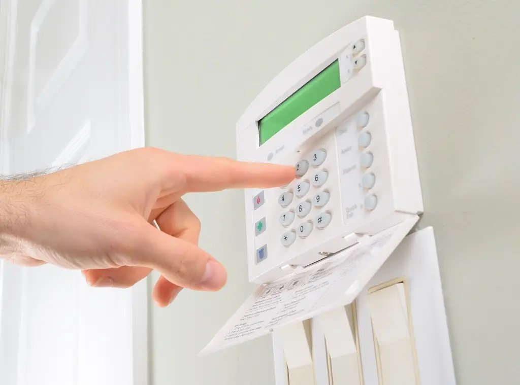 A technician replacing a backup battery inside an open alarm system control panel.
