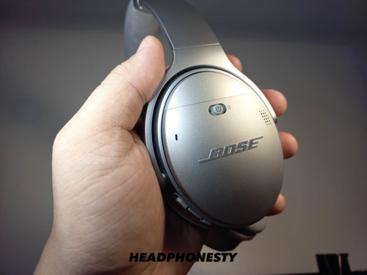 Close up of hands interacting with headphone buttons to perform a factory reset.