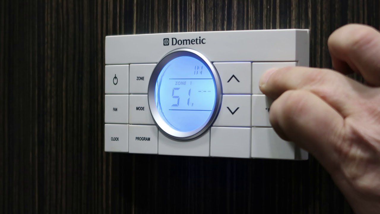 Two different models of RV thermostats mounted side by side on a wall.