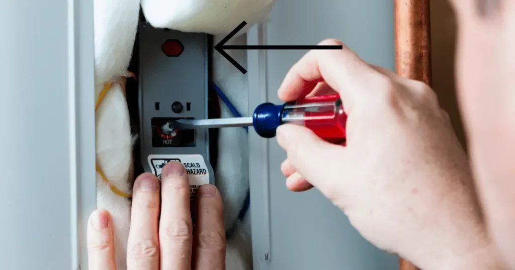 Hands opening the access panel of a water heater to reach the reset button.