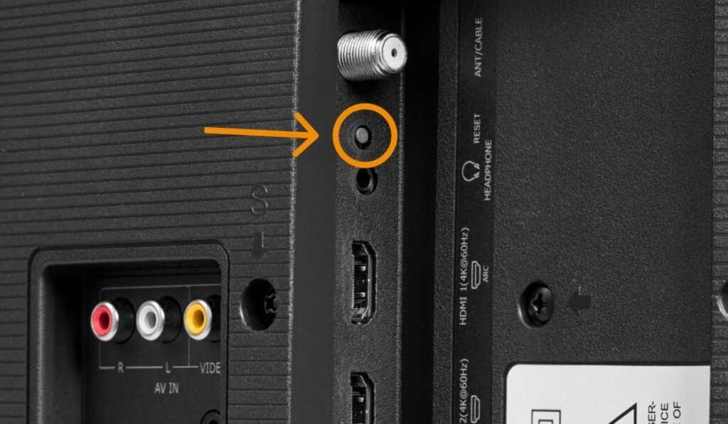 A close-up view of the physical reset pinhole on the back of a TV.