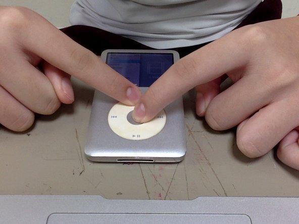 Two thumbs pressing the Menu and center buttons on an iPod Classic device.