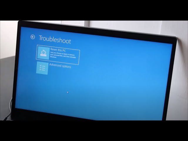 Hands typing on a Lenovo IdeaPad while choosing reset settings on the screen.