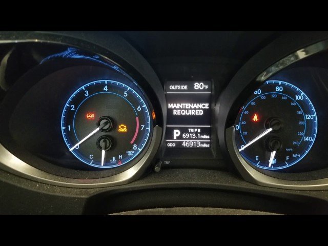 A hand pressing the trip meter reset knob on a Corolla dashboard.