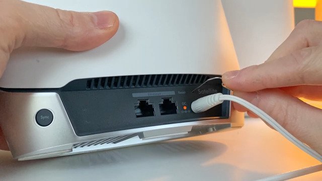 A metal paperclip is inserted into the reset port of an Orbi router.