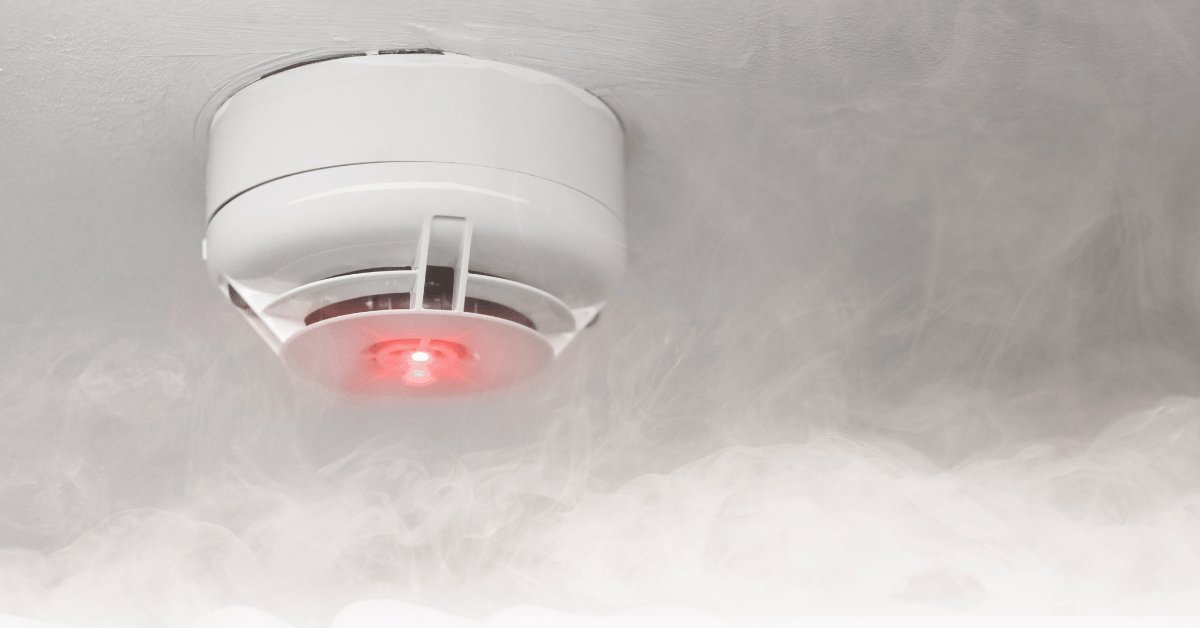 Gently vacuuming dust from a smoke detector to prevent false alarm triggers.